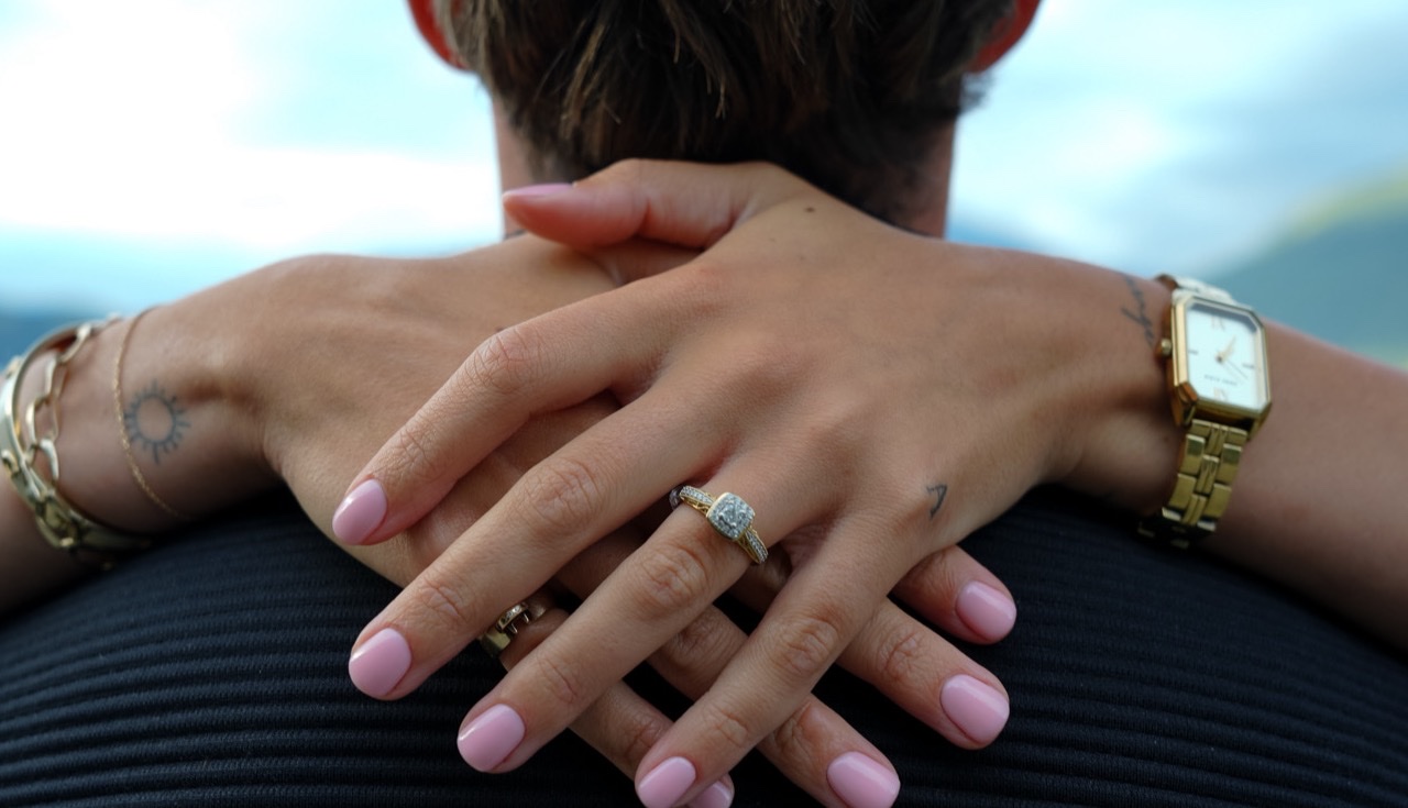 A couple holding hands at the lakeshore after their engagement